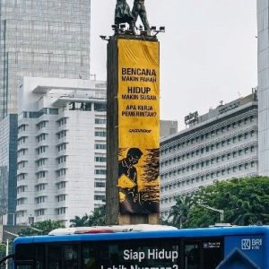 Spanduk protes Greenpeace soal krisis iklim di Bundaran HI dengan latar gedung Sinar Mas dan bus TransJakarta