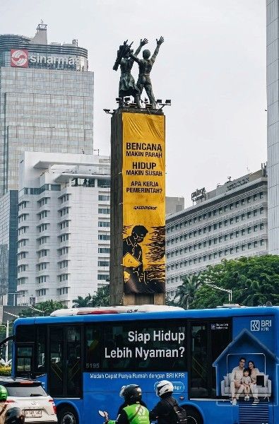 Spanduk protes Greenpeace soal krisis iklim di Bundaran HI dengan latar gedung Sinar Mas dan bus TransJakarta
